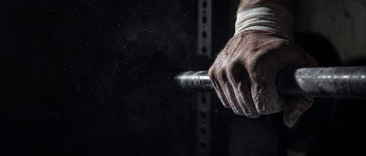 A chalked hand gripping a loaded barbell, lit from one side in a dark gym.